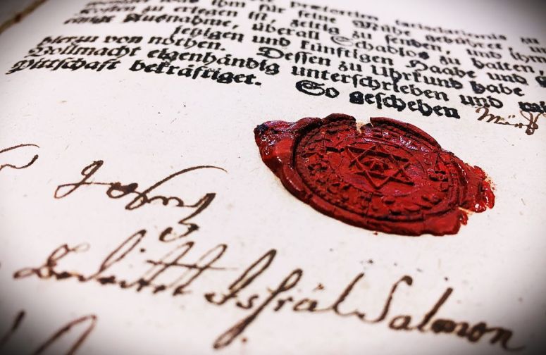 Close-up of an aged document featuring handwritten text and a red wax seal with a Star of David.
